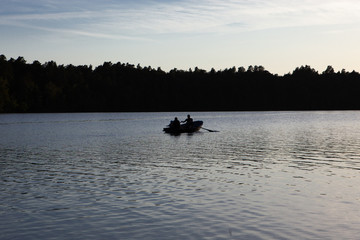 Family in a boat at sunset on the calm waters of a lake and behind a forest enjoying life