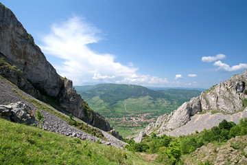 Sunny summer day, white clouds over mountain peak, where tourists climb to conquer fear, find courage and develop lateral thinking skills to overcome the difficulty of climbing a mountain. Small road