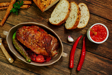 Baked pork loin  in ceramic form with fork, knife and homemade rustic bread on dark rustic background. Roasted pork served with grilled vegetables and tomato sauce. Cozy village dinner..