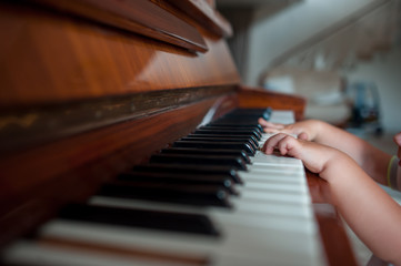 The boy's little hands play the piano in the middle of the room