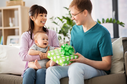 family, parenthood and fathers day concept - happy mother with baby boy giving birthday present to father at home