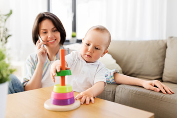 family, child and motherhood concept - happy baby boy playing developmental toy and mother calling on smartphone at home