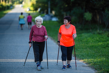 An elderly woman is engaged in Nordic walking with her adult daughter.