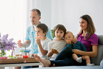 Beautiful young family with three children, eating pizza at home and watching TV