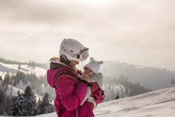 Fototapeta na wymiar Young mother, carrying her baby boy in sling, climbing on peak wintertime, Austrian Apls