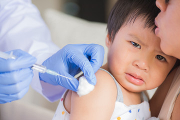 Doctor giving an injection vaccine to a girl. Little girl crying with her mother on background.