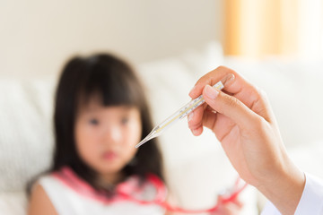 Doctor holding digital thermometer to measuring temperature of her ill kid and sick little girl with stethoscope in background.
