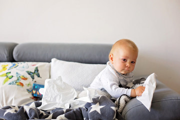 Sick little toddler boy, sitting on a couch in living room