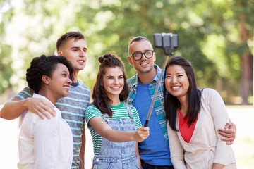 people, friendship and international concept - happy smiling young woman and group of happy friends taking picture by selfie stick in park