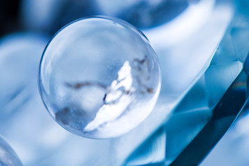 Macro shot of transparent crystal balls with colorful ornaments and sun reflections in it, on turquoise glass pad. Fortune telling. Love, money, luck, success.