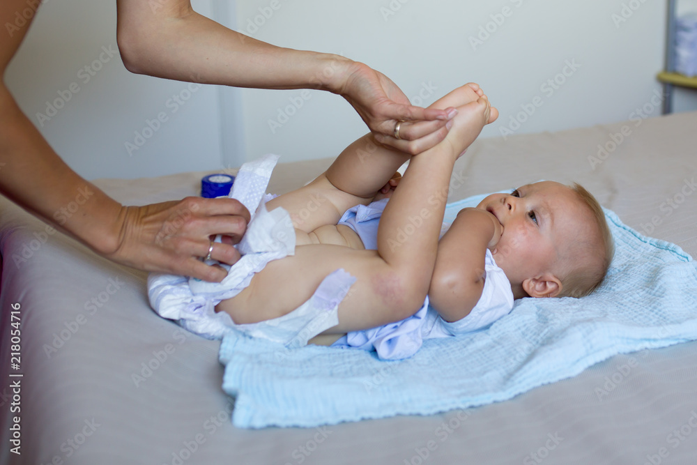 Poster Mother putting diaper on her happy baby in nursery.