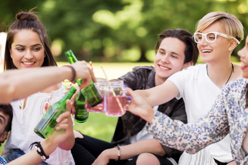 leisure, people and celebration concept - happy friends clinking non alcoholic drinks at summer park
