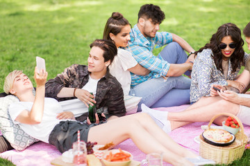 friendship, leisure, technology and people concept - group of friends with smartphones and non alcoholic beer chilling on picnic blanket at summer park