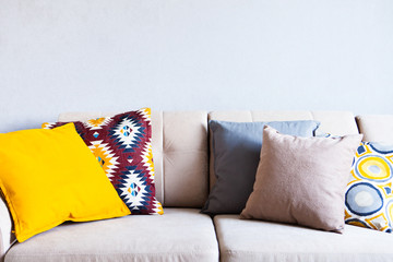 Multi-colored pillows on a beige fabric sofa, the concept of home comfort and cozy, copy space, close up
