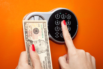 Hand with 10 dollars, finger on digital lock of safe