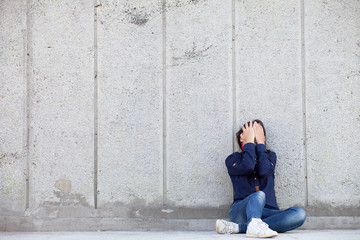 A teenage girl with depression sits alone on a concrete wall background