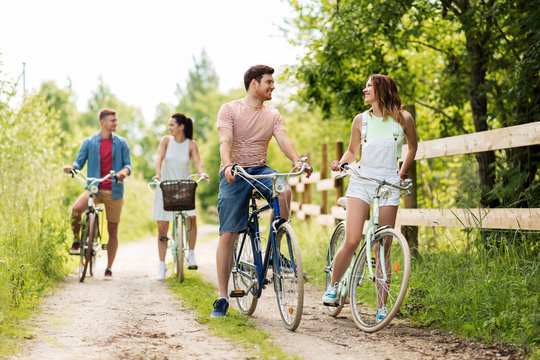 people, leisure and lifestyle concept - happy young friends with fixed gear bicycles on road in summer