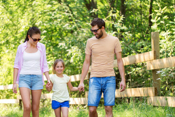 Fototapeta premium family, leisure and people concept - happy mother, father and little daughter walking in summer park