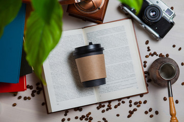 Coffee take away a disposable glass. On the table the student (or photographer) the stack of books, cezve, grinder, phone, camera and a coffee to go. Top view.