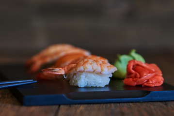 Traditional japanese food. Close up of sashimi sushi set with, prawns, soy sauce, wasabi, ginger and chopsticks. Sushi menu. Set sashimi are on a black wooden board. Japanese cuisine. Selective focus.