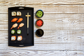 Full sushi set with different types of rolls and sashimi, chopsticks and soy sauce on side. Set of japanese rolls with seasoning on black wooden plate on white background. Top view with copy space.