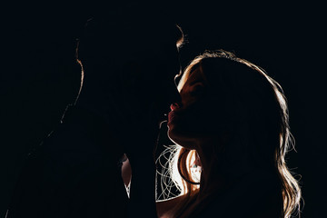 silhouettes of sensual heterosexual couple kissing in dark