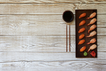 Full sushi set with different types of rolls and sashimi, chopsticks and soy sauce on side. Set of japanese rolls with seasoning on black wooden plate on white background. Top view with copy space.