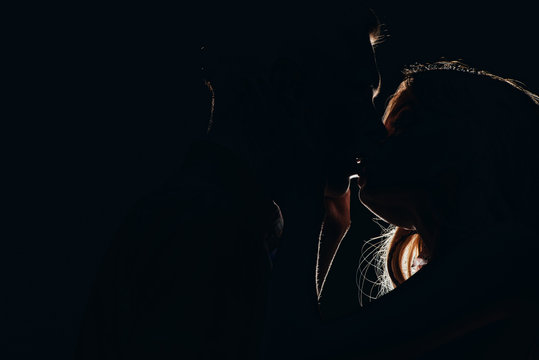 silhouettes of passionate heterosexual couple kissing in dark