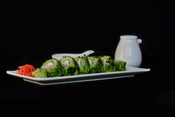 Sushi set: sushi rolls on white porcelain plate with chopsticks and soy sauce. Traditional japanese food. Sushi menu.  Roll with salmon, avocado, cucumber and sea kale on black background..