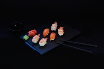 Sashimi sushi set on a black wooden board for sushi on black background. Close up of sashimi sushi with prawns. Traditional japanese food. Sushi menu. Delicious dinner in the restoran. Selective focus