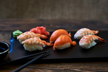 Food sushi background. Close up of sashimi sushi set with chopsticks and soy.  Japanese food restaurant,  sushi on dark background. Fresh made sushi set with salmon, prawns, wasabi and ginger.