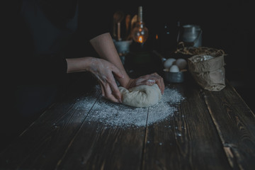 Female hands making dough for pizza. Woman preparing bread dough on table. Making bread, retro style imagery. Fresh raw dough ball on brown table. Concept of healthy home food. Soft focus.