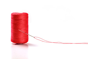 A photo of a needle with a red thread and a spool on a white background