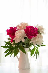White and pink peonies in vase on white table