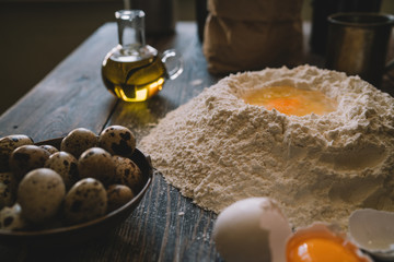 Food, cooking and baking concept. Ingredients for dough. Eggs, flour, rolling pin and eggshells on brown table. Dough preparation recipe bread, pizza or pie. Working with bakery cooking. Soft focus.