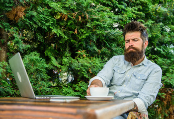 Man bearded hipster make pause for drink coffee and think while sit with laptop. Guy drinks coffee...