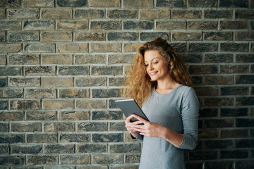 Portrait of woman using tablet in front of brick wall.