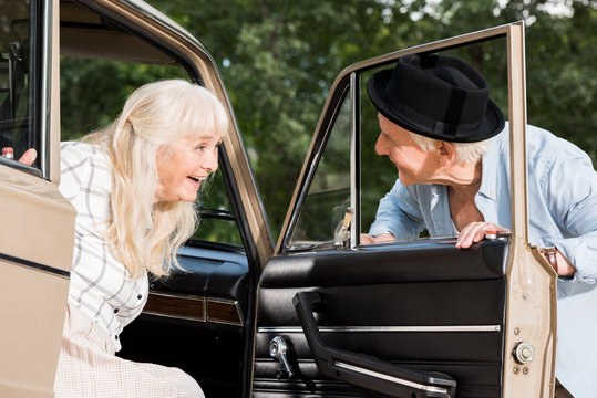 Smiling Senior Man Opening Car Door In Front Of Woman