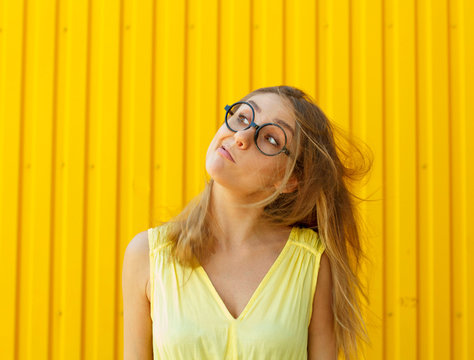 Portrait of a joyful girl wearing toy funny glasses blowing away her hair from face over yellow background at daylight