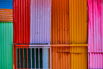 Background and texture of old color corrugated metal sheet. Sheets of colorful corrugated iron overlap in an old, roughly constructed wall.