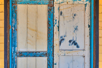 Weathered, wooden door in an old house. Old wooden door with leaving paint. Part old house yellow wall with blue and white door. Weathered painted wooden surface. Vintage color.Grunge wood texture.