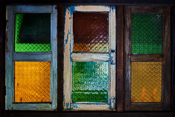 Old wooden windows with color stained glass. Colorful glass window in wooden worn frame.  Glasses of green, blue, and yellow color separated by a line. Window background and texture. .