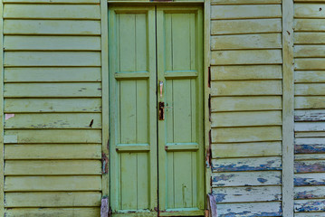 Old broken green shut door in an abandoned house with wooden panels and peeling cracked surrounding walls painted green. Abandoned facade with peeling green paint decaying facade. Abstract background.