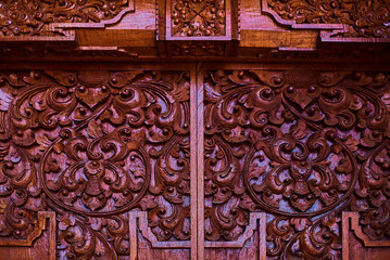 Traditional carving balinese style door. Detail of a red door with vignetting depicting floral pattern. Handmade vintage wooden carving door.  Magnificently and ornate entrance door to temple.
