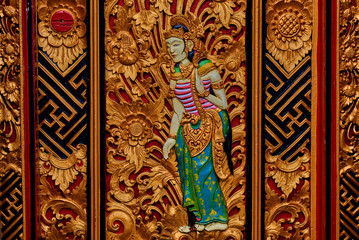 Traditional carving balinese style door.Detail of a red and gold door with vignetting. Handmade vintage wooden carving door. Magnificently and ornate entrance door to temple. Balinese temple ornament.