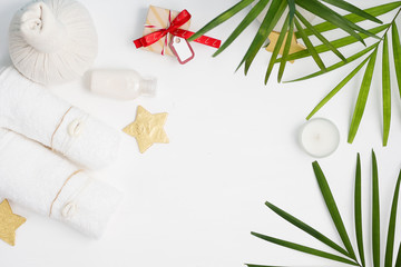 Christmas spa tropical mockup: white towels, Thai massage bags, golden stars and green fern leaves with gift boxes on background. New year gift concept. Text space