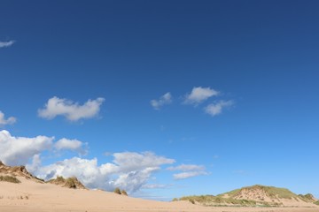 Fototapeta na wymiar Little fluffy white clouds in blue sky over sand dunes