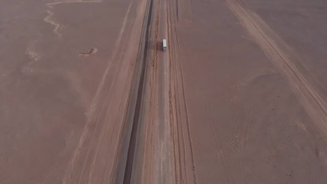 Aerial view of truck driving road leading to horizon in Atacama desert Chile. Drone tilting up cinematic filming vehicle and vast empty sand desert landscape during cloudy day.