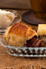 Pastry stuffed with meat sausages, white cream in a glass gravy boat, napkins of coarse cloth, all on a wooden background.