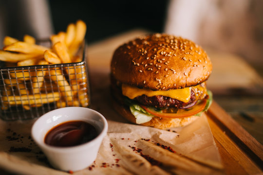 Tasty beef burger with fresh fries. Concept of fast food. Grilled beef burger with lettuce and mayonnaise served on pieces of brown paper on rustic wooden table. An american burger with fried potatoes